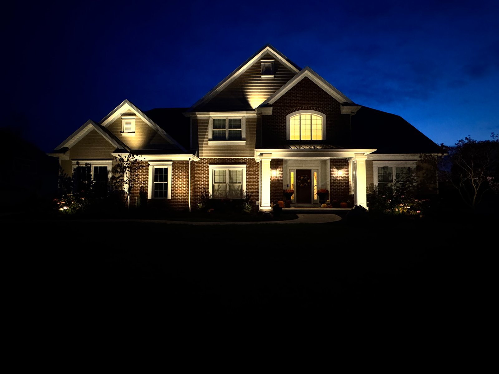 Two-story brick home with architectural uplighting at dusk
